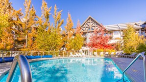 A swimming pool with lounge chairs and a building with a distinctive architectural style in the background. - SKI IN/OUT, close to gondola and village - 1 bd, Hot Tubs/pool (Whistler)