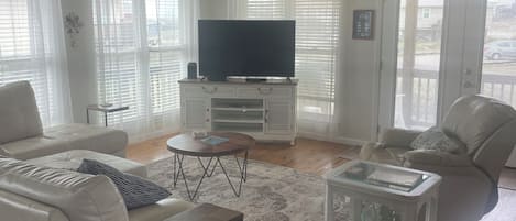 A living room with a white sofa, a coffee table, a TV on a stand, and a ceiling fan.
