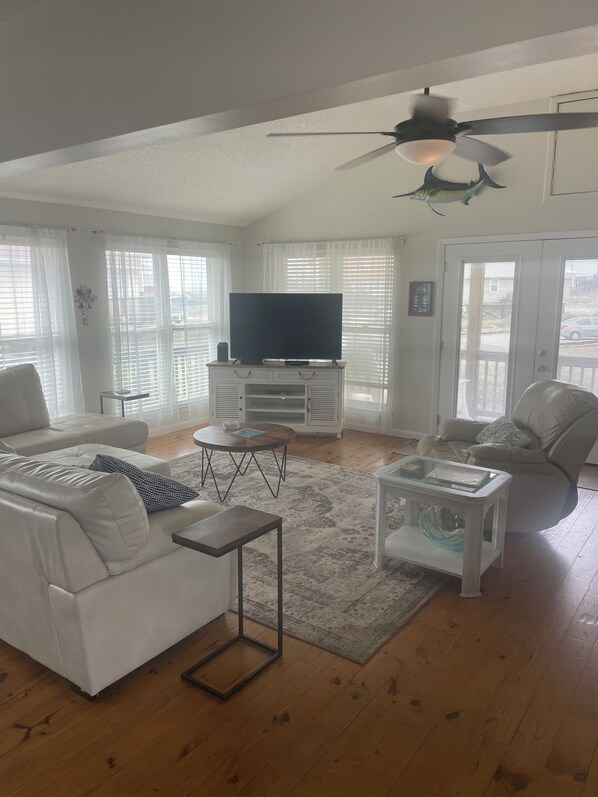 A living room with a white sofa, a coffee table, a TV on a stand, and a ceiling fan. - Ocean View Beach Cottage/3BR 2BA/Steps Away From the White, Sandy Beach! (Dauphin Island)