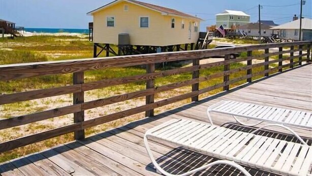 Una pasarela de madera que conduce a una casa amarilla con un pequeño balcón, con vista a una playa.