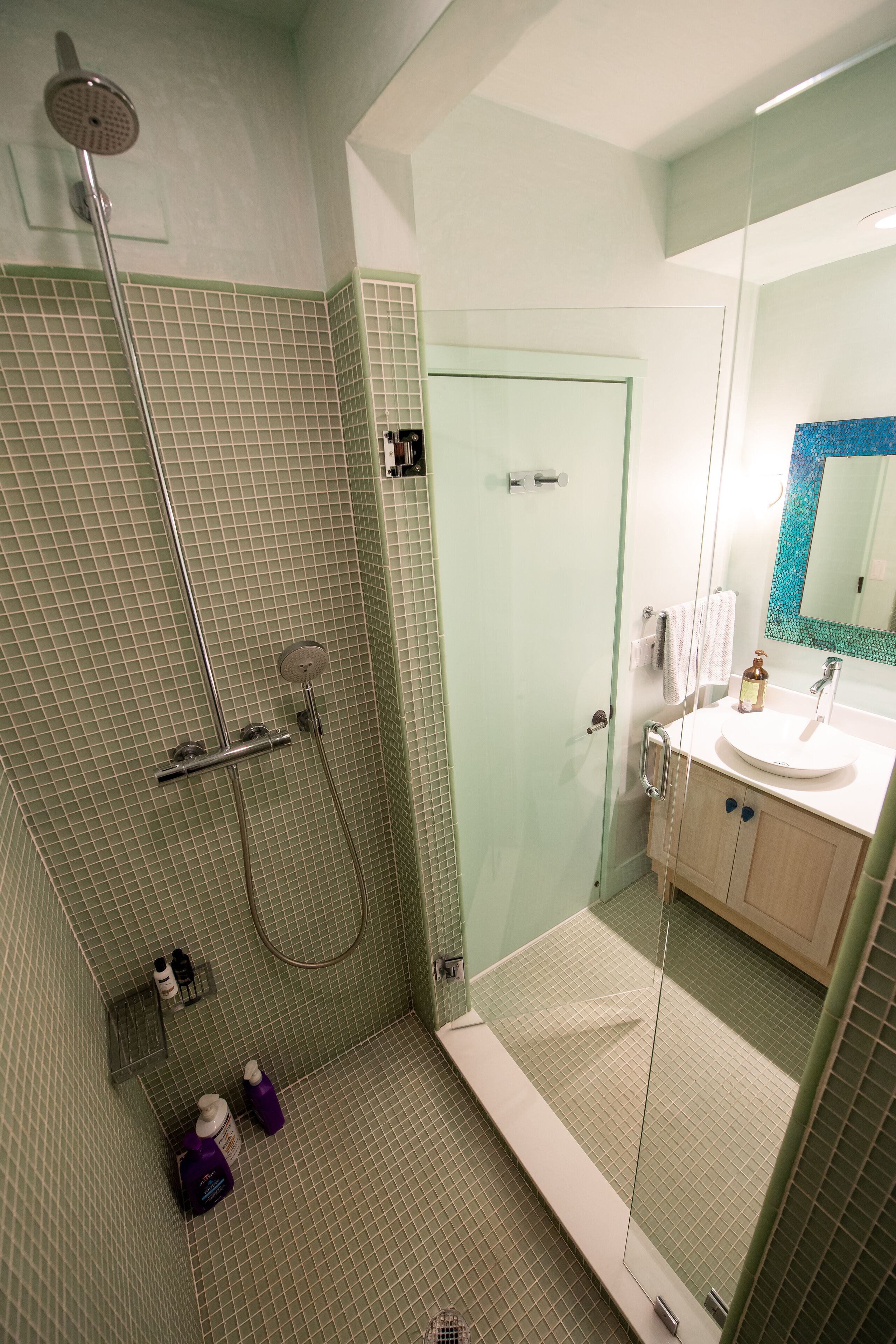 Une salle de bain moderne avec une douche à l’italienne en verre, un lavabo avec un miroir et un sol carrelé.