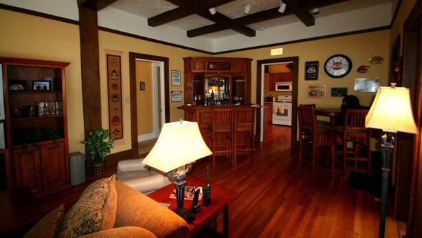 A cozy living room with wooden floors, a sofa, a coffee table, and a bar area with a refrigerator and microwave. - AWESOME STURGIS HOME FOR STURGIS RALLY (Sturgis)