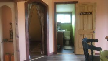A hallway with a wooden door, a small bathroom with a toilet and sink, and a chair in the foreground.