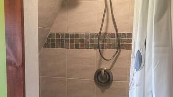 Un espace douche équipé d’un pommeau de douche à main, d’un panneau de commande mural et d’un sol carrelé.