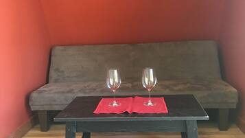 A small room with a dark wooden table, two wine glasses on a red cloth, and a grey sofa against a red wall.