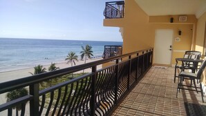 Un balcón con vista a la playa y el océano, una puerta con un letrero de salida y mobiliario exterior.