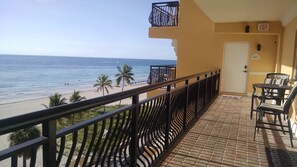 A balcony with a view of the beach and ocean, a door with an exit sign, and outdoor furniture. - Oceanview Condo with  Pool – Right on the Hollywood Beach Boardwalk! (Hollywood)