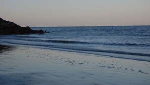 En strand med vågor som rullar in mot land, en klar himmel och klippiga utskjutande partier.