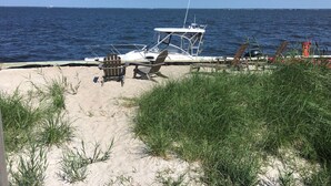 Una platja amb dues cadires Adirondack, un vaixell i una zona de sorra amb gespa.
