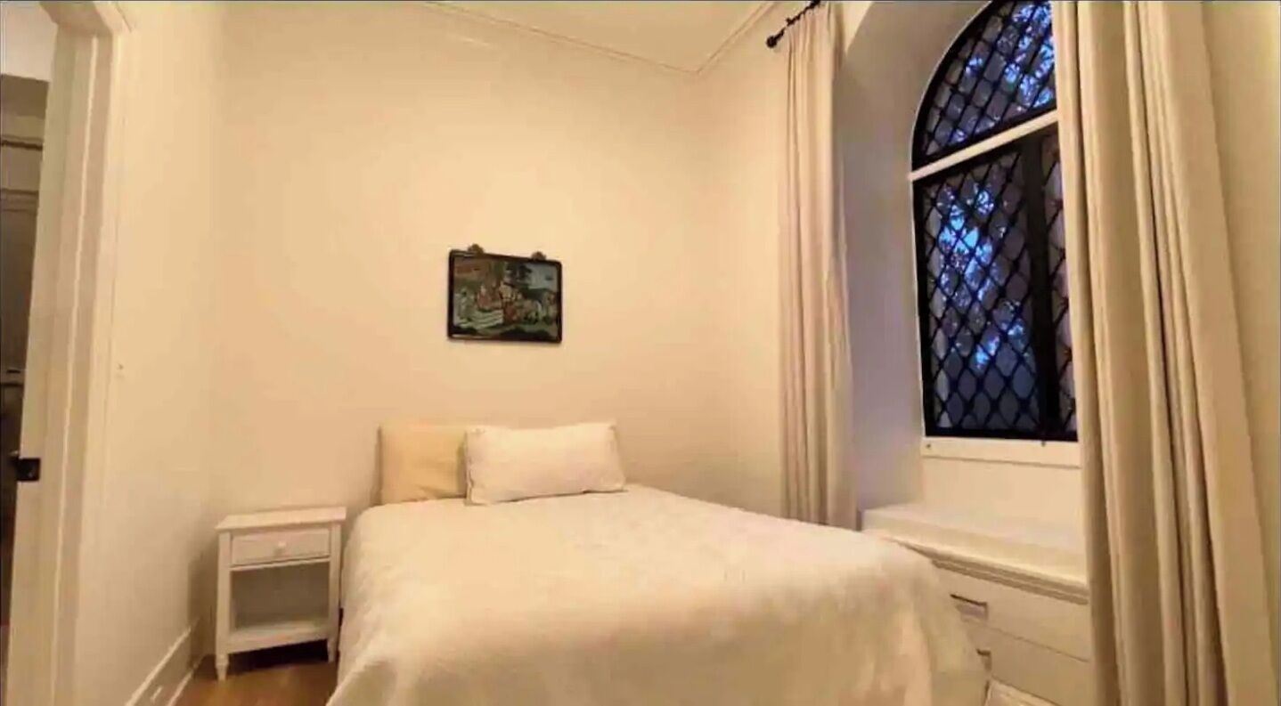 A bedroom with a bed, a nightstand, a dresser, a window with curtains, and a wall-mounted picture.