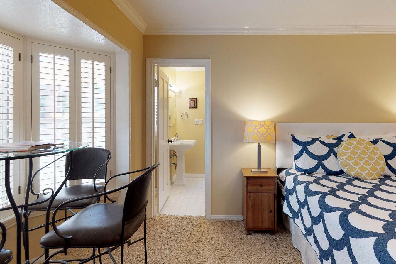 A bedroom with a bed, bedside table, lamp, and a chair.