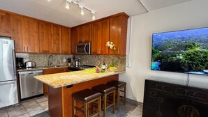 Une cuisine moderne avec des meubles en bois, des comptoirs en granit, un îlot central doté de tabourets, des appareils en acier inoxydable et une grande fenêtre offrant une vue panoramique.