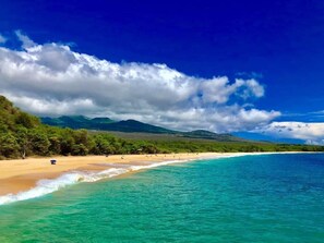 A beach with clear turquoise water, a sandy shore, and a backdrop of green hills under a partly cloudy sky. - Kihei Beach Condo, Romantic Kamaole II (Kihei)