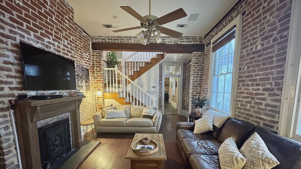 A living room with a fireplace, leather sofas, a wooden coffee table, and a TV mounted on the brick wall. - Stylish Escape in Historic Warehouse District (New Orleans)