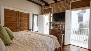 A bedroom with a large bed, wooden wardrobe, and a television mounted on the brick wall. - Stylish Escape in Historic Warehouse District (New Orleans)