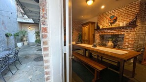 A brick fireplace with a mantel, a wooden table with benches, and a view of the outdoor patio area. - Stylish Escape in Historic Warehouse District (New Orleans)