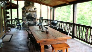 A wooden deck with a stone fireplace, outdoor seating, and a view of the forest. - Double-Decker Dock - Beautiful View (Blairsville)