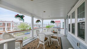 Une véranda couverte, aménagée avec des meubles en osier, une table et des jardinières suspendues.