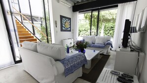 A modern living room with a white sofa, a coffee table, and a TV stand with remote controls. - Architectural/Minimal Villa in Forte dei Marmi, Roma Imperiale (Forte dei Marmi)