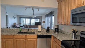 A kitchen with granite countertops, wooden cabinets, a dishwasher, a coffee maker, and a microwave. - Right on the Beach,  Ocean View, Modern 2BR/2B, 2 balconies (Cocoa Beach)