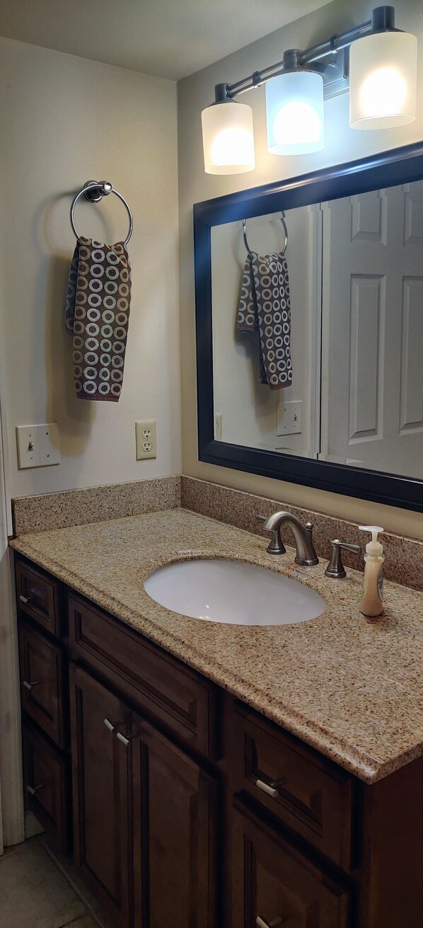 A bathroom with a granite countertop sink, a large mirror, and a towel rack with patterned towels. - Right on the Beach, Ocean View, Modern 2BR/2B, 2 balconies (Cocoa Beach)