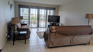 A living room with a sofa, a TV, and a table with lamps. - Right on the Beach,  Ocean View, Modern 2BR/2B, 2 balconies (Cocoa Beach)