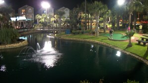 A nighttime view of a swimming pool with surrounding greenery and buildings. - Beautiful Efficiency Condo Across The Street from Beach. Great Pool & Deck Area. (North Myrtle Beach)