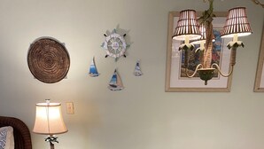 A dining area with a glass table and wicker chairs, a clock, decorative wall art, and a lamp. - Beautiful Efficiency Condo Across The Street from Beach. Great Pool & Deck Area. (North Myrtle Beach)
