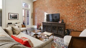 Una sala de estar con una pared de ladrillo, un televisor sobre un mueble y un sofá con un cojín rojo.