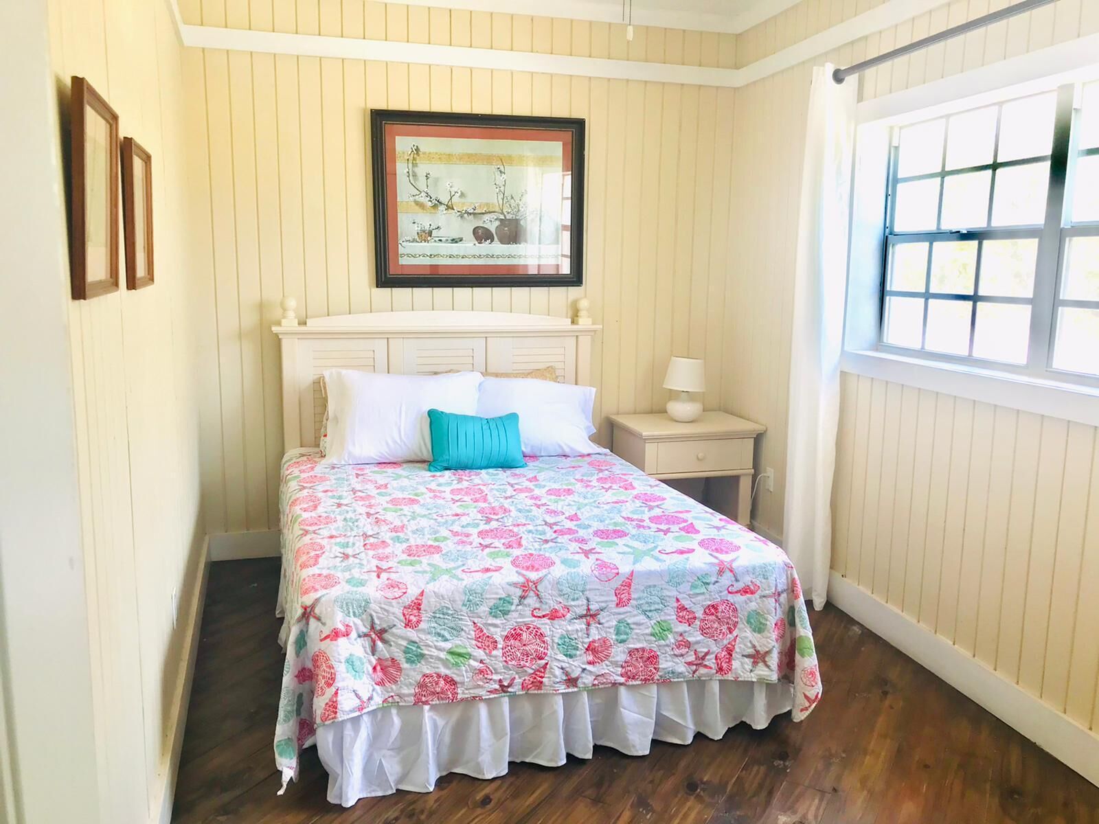 A bedroom with a bed, a nightstand, a framed picture, and a window.