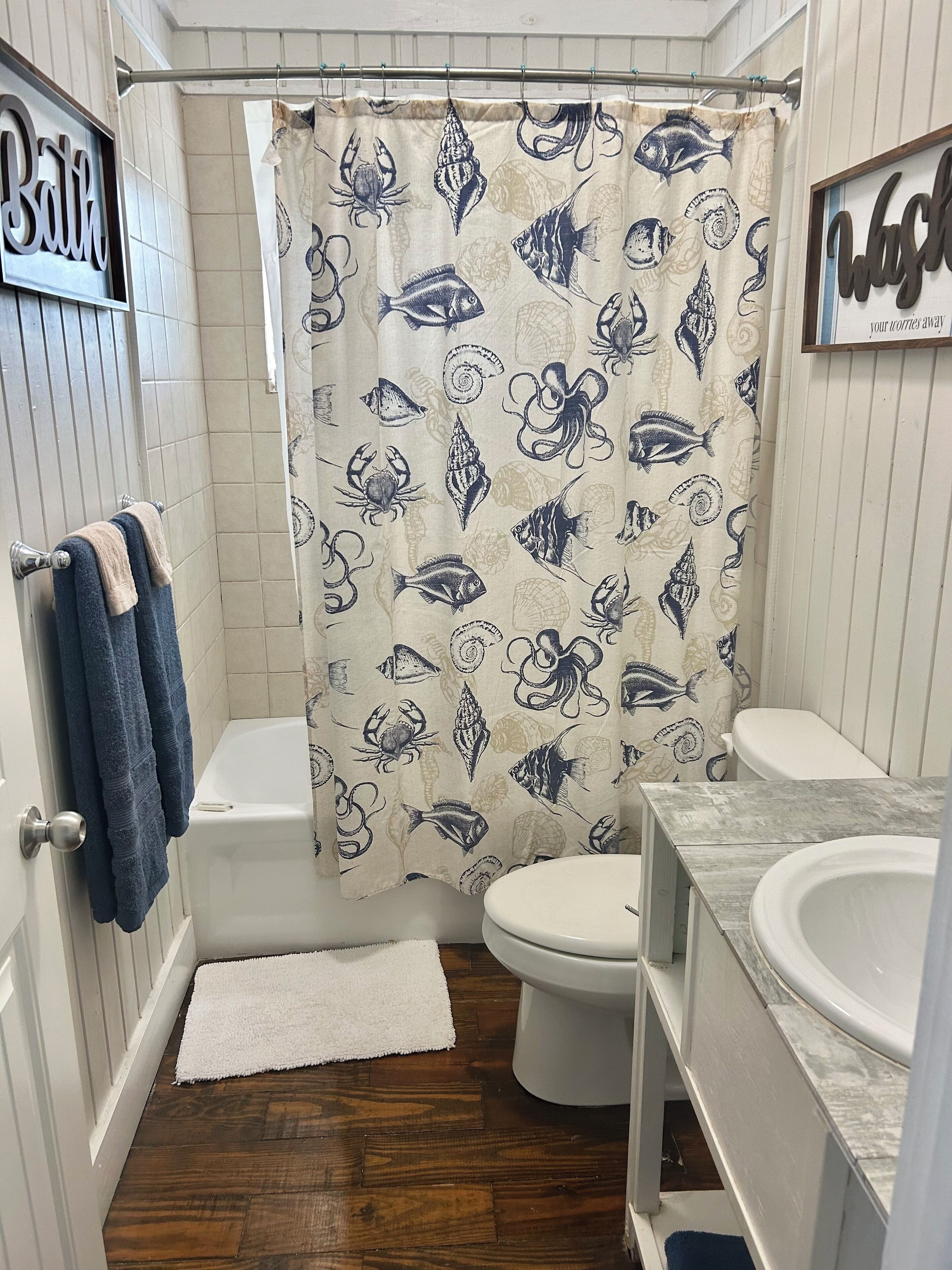 Un baño con cortina de ducha con motivos marinos, un inodoro, una bañera y un lavabo.
