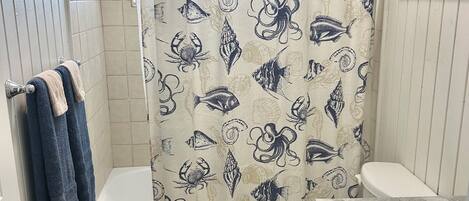 Un baño con cortina de ducha con motivos marinos, un inodoro, una bañera y un lavabo.