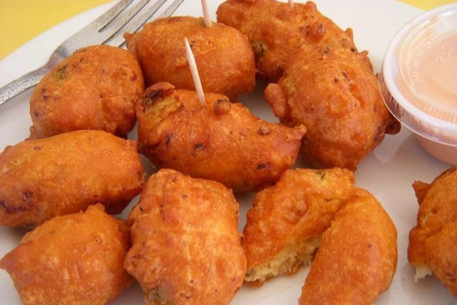 Un plato de comida frita, posiblemente buñuelos, con un tenedor y un recipiente de salsa para mojar.
