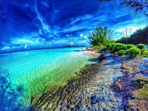 A beach with clear turquoise water, rocky shoreline, and green vegetation.