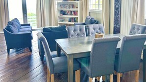 Ein geräumiges Wohnzimmer mit einem großen Sofa, einem Esstisch mit Stühlen, einem Bücherregal und einem Deckenventilator.