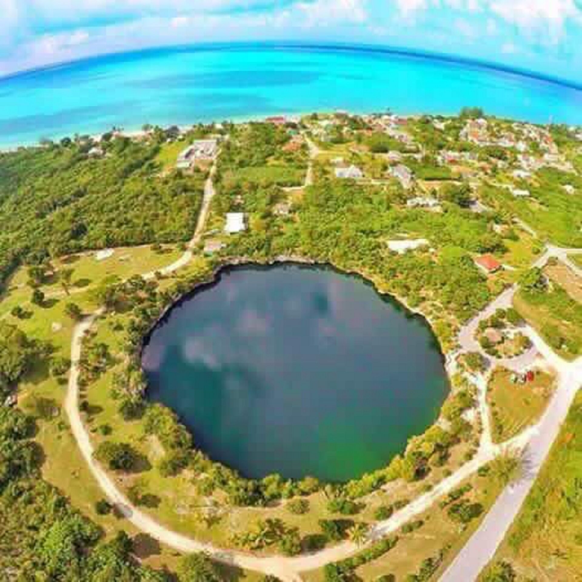 A circular lake surrounded by greenery and a few buildings.