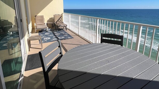 A balcony with a table and chairs, overlooking the ocean. - Crystal Shores, Gulf Shores. Family Friendly Beachfront Condo w/ Pool,GYM & more (Gulf Shores)