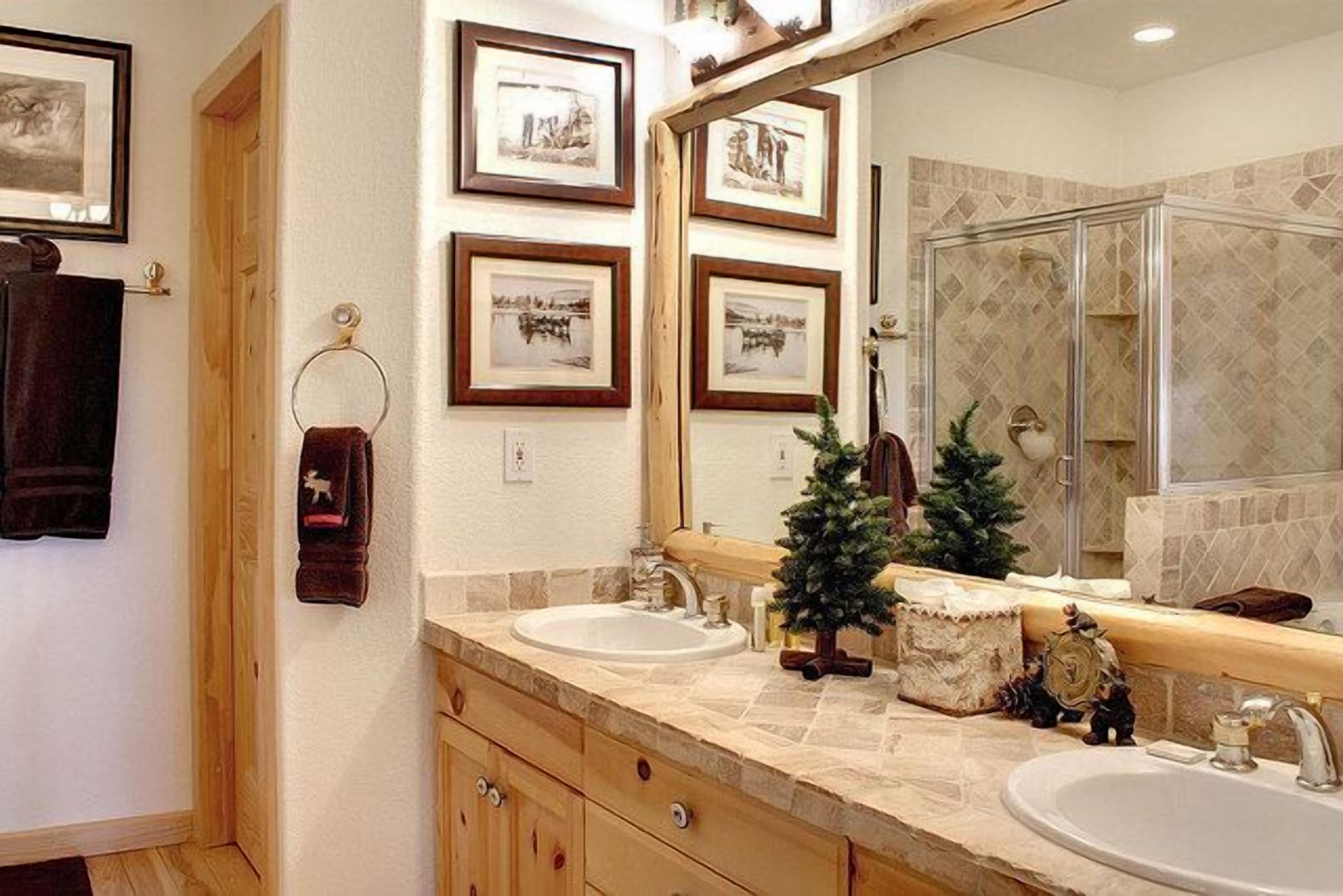 Une salle de bain avec deux lavabos, un grand miroir, des tableaux encadrés accrochés au mur et un petit sapin de Noël.