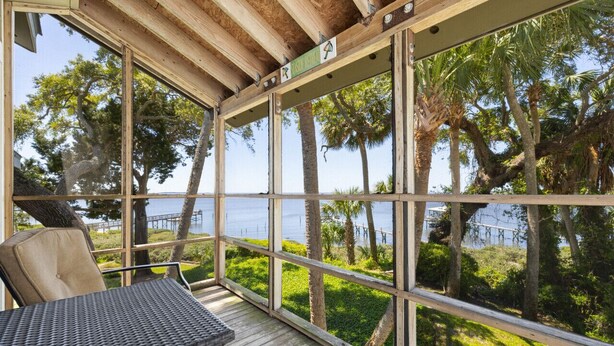 A covered outdoor seating area with a view of the sea and palm trees. - Serenity by the Sea at Whitman Point. Gulf front and Screened Porches (Cedar Key)