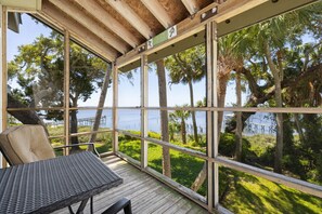 A covered outdoor seating area with a view of the sea and palm trees. - Serenity by the Sea at Whitman Point. Gulf front and Screened Porches (Cedar Key)