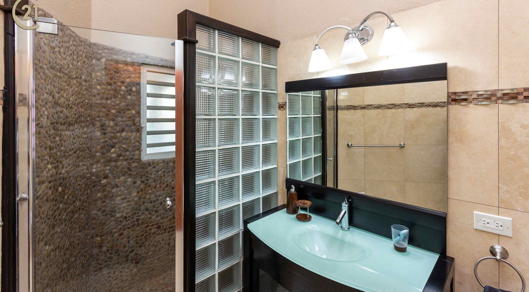 A bathroom with a glass shower enclosure, a glass sink, and a large mirror.