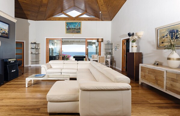 Een ruime woonkamer met een grote hoekbank, houten vloeren en uitzicht op buiten.