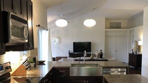 A modern kitchen with dark cabinetry, stainless steel appliances, a central island with a sink, and a flat-screen TV mounted above the island.