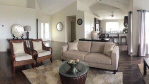 A spacious living room with a sofa, chairs, a glass coffee table, and a dining area with a glass table.