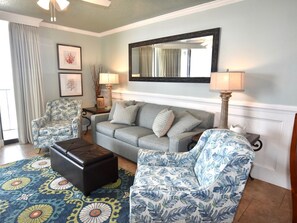 A living room with a grey sofa, patterned armchairs, a coffee table, and a large mirror on the wall. - Beachfront 2BR/2BA | Direct Gulf Front | Resort Amenities | Sleeps 8 (Orange Beach)