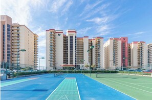 Un edificio residencial de varios pisos con balcones, cancha de tenis y zona de estacionamiento.