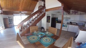 A dining area with a wooden table set for four, a staircase, and a kitchen in the background.