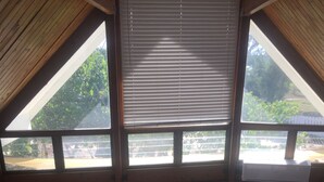 A spacious attic room with large windows, wooden beams, and a view of the outdoors.