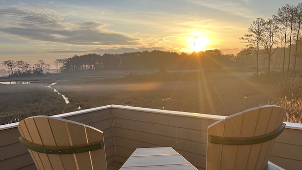 A deck with two Adirondack chairs and a table, overlooking a landscape with trees and a body of water during sunset. - GREAT LOCATION!  Million dollar view of the Salt Pond  (Bethany Beach)