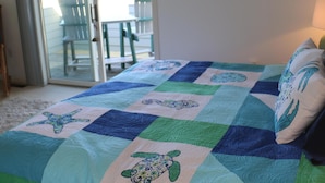 A bedroom with a bed covered in a quilt, a sliding glass door leading to an outdoor area, and a framed picture on the wall. - GREAT LOCATION!  Million dollar view of the Salt Pond  (Bethany Beach)